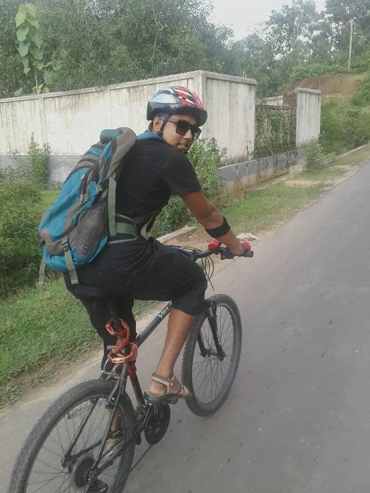 Sajjad holding a bicycle with a backdrop of a lush tea garden